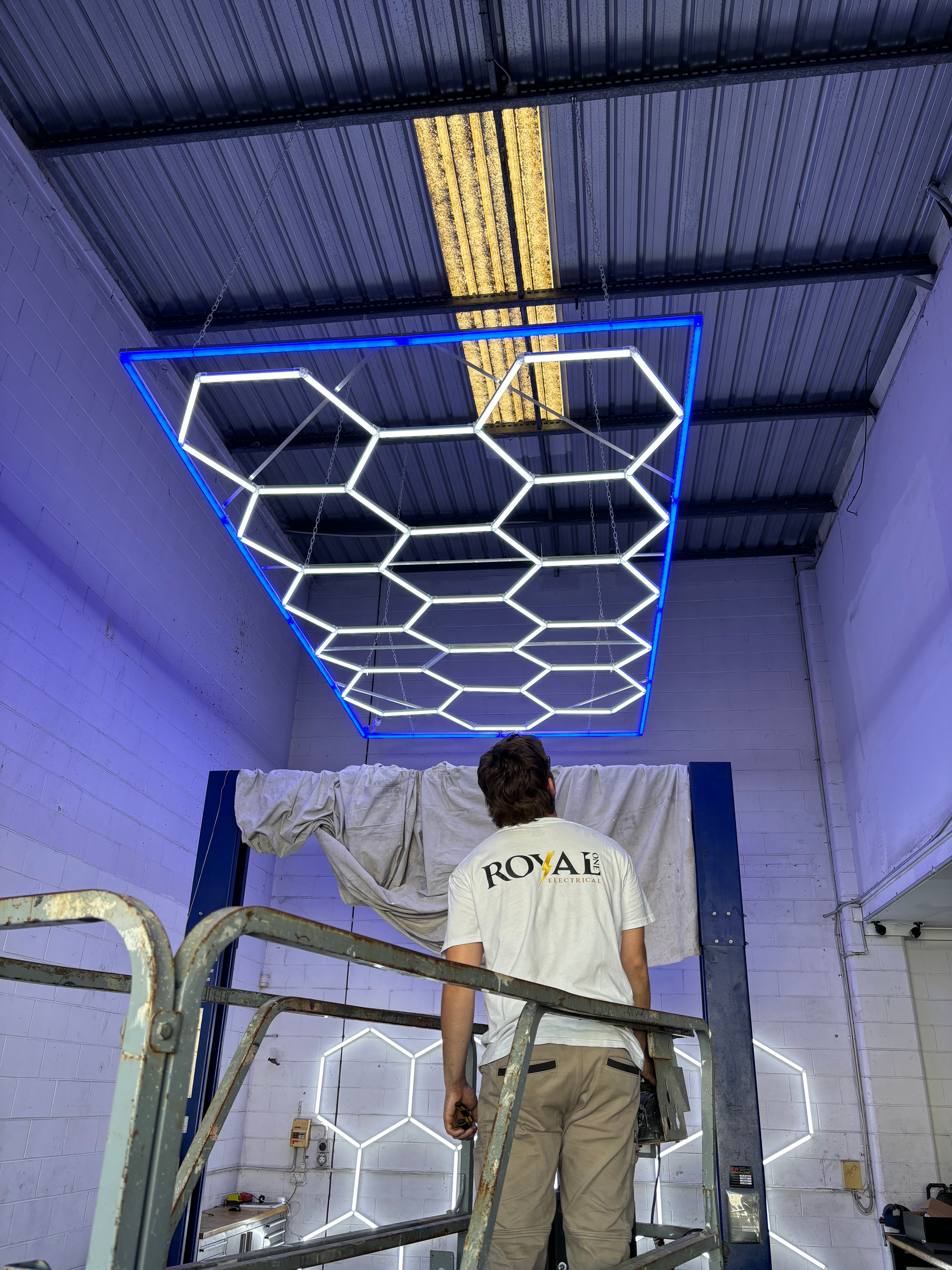 A man is standing on a ladder in a warehouse looking up at the ceiling.