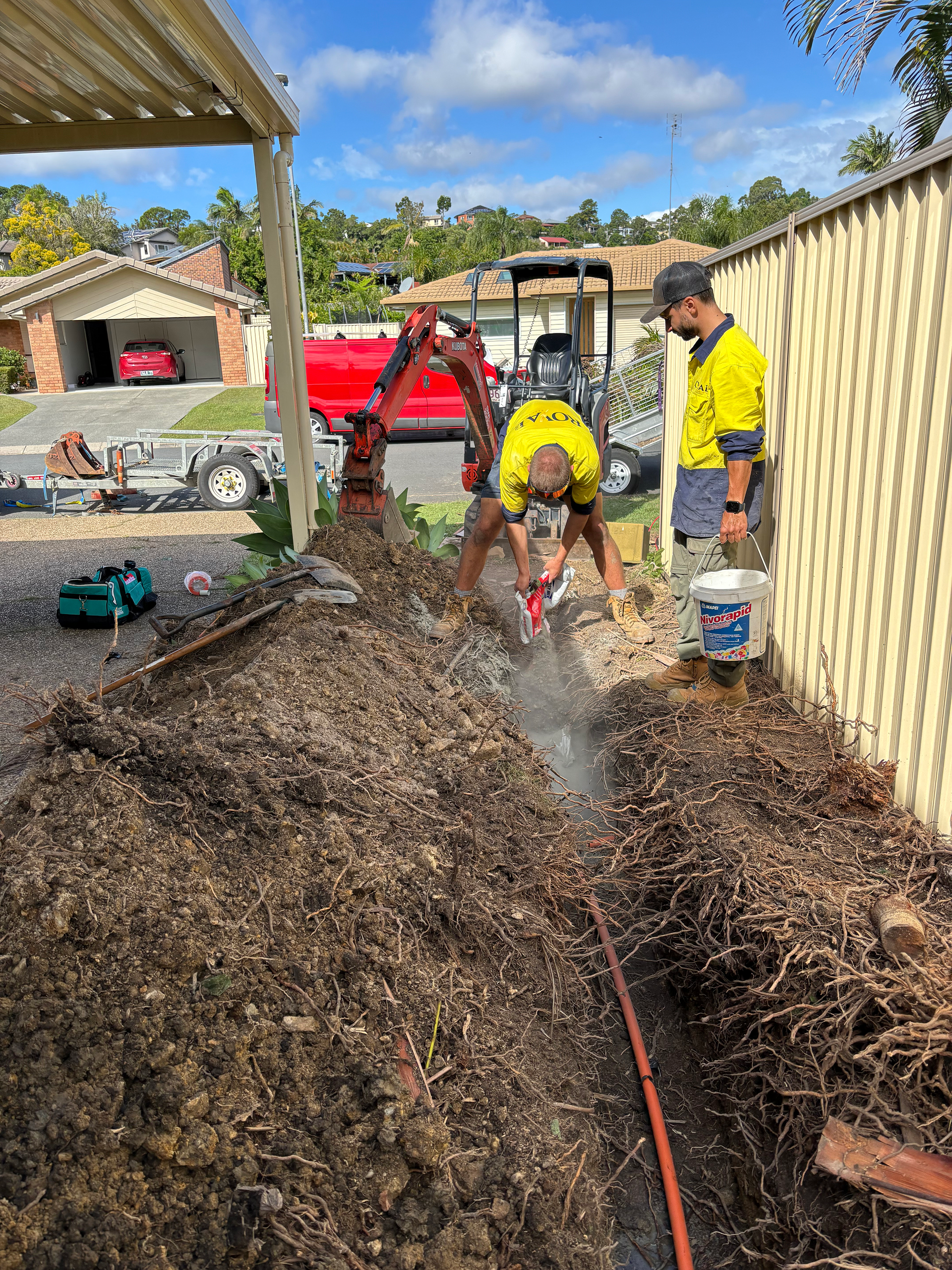 Two men are digging a hole in the ground in front of a house.