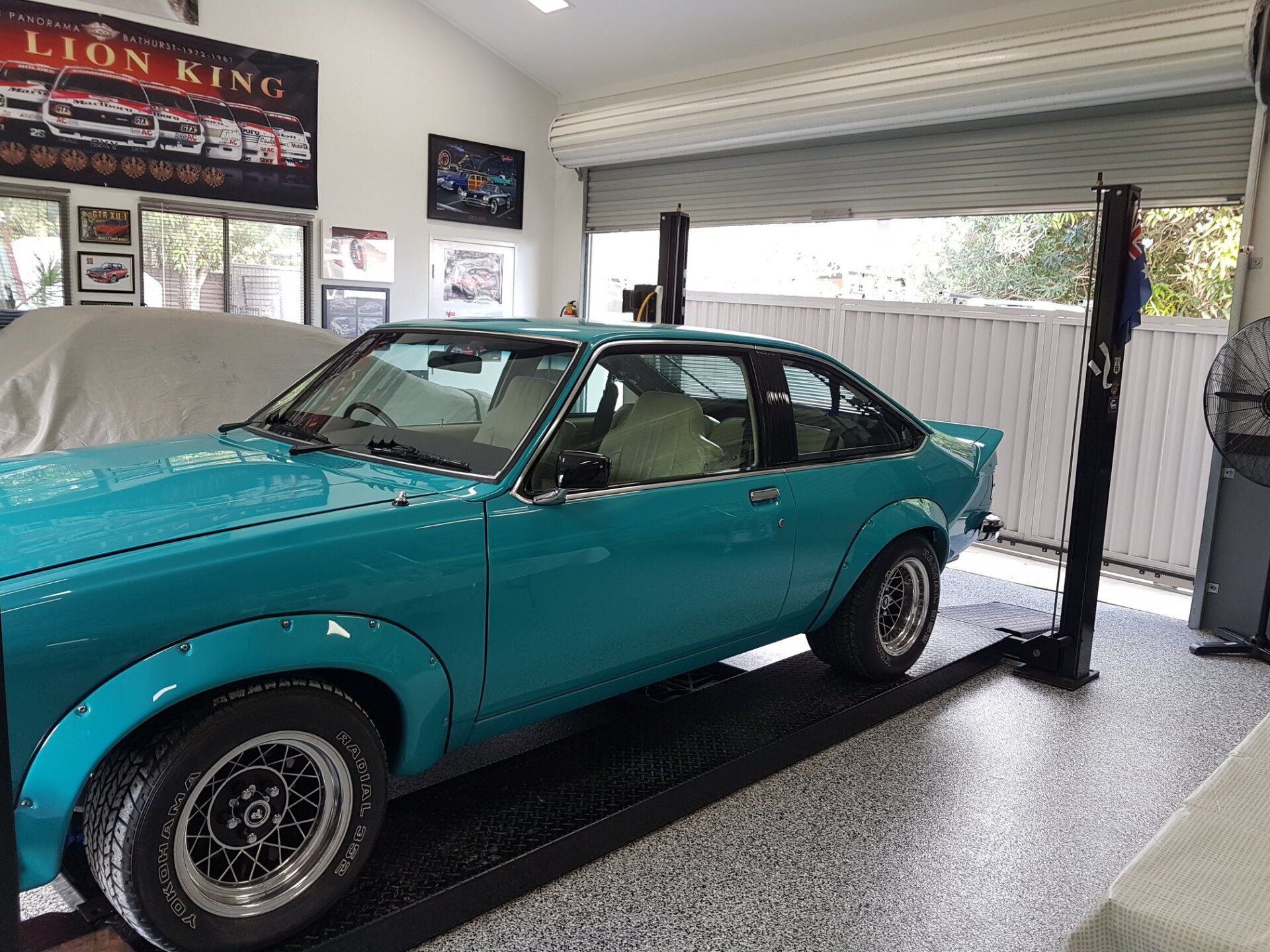 Teal Vintage Car on a Black Lift in a Garage With Memorabilia and a White Fence — Motorhead Garage in Tweed Heads, QLD