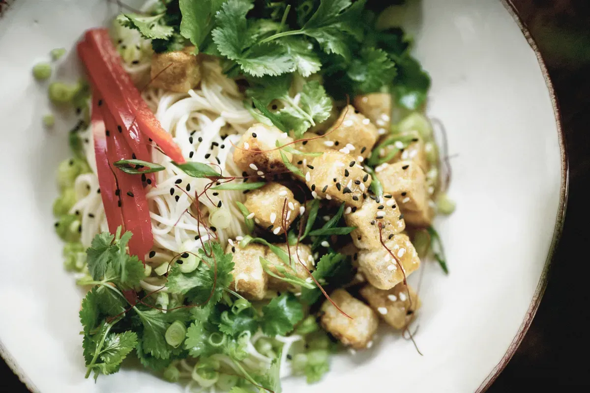 A close up of a plate of food with noodles and vegetables on a table.