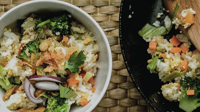 A bowl of rice and vegetables with a wooden spoon on a table.