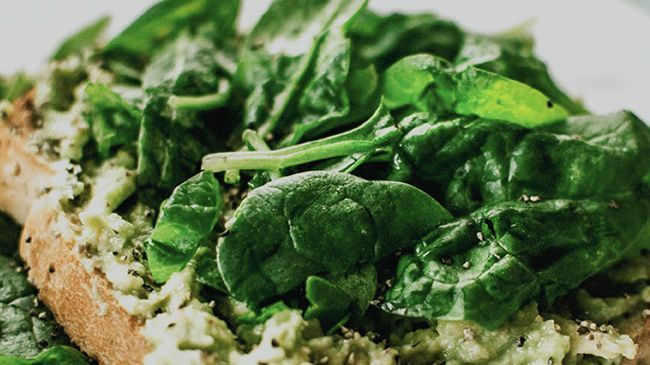 Two slices of toast with spinach and avocado on a white plate.