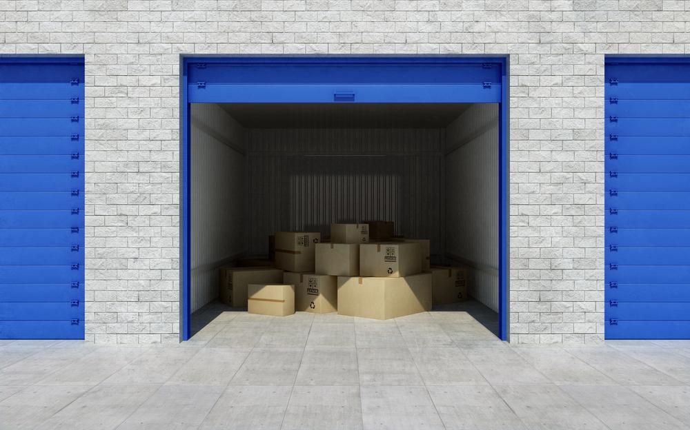 A Stack Of Cardboard Boxes In A Garage With Blue Doors — Raymond Terrace Public Storage In Thornton, NSW