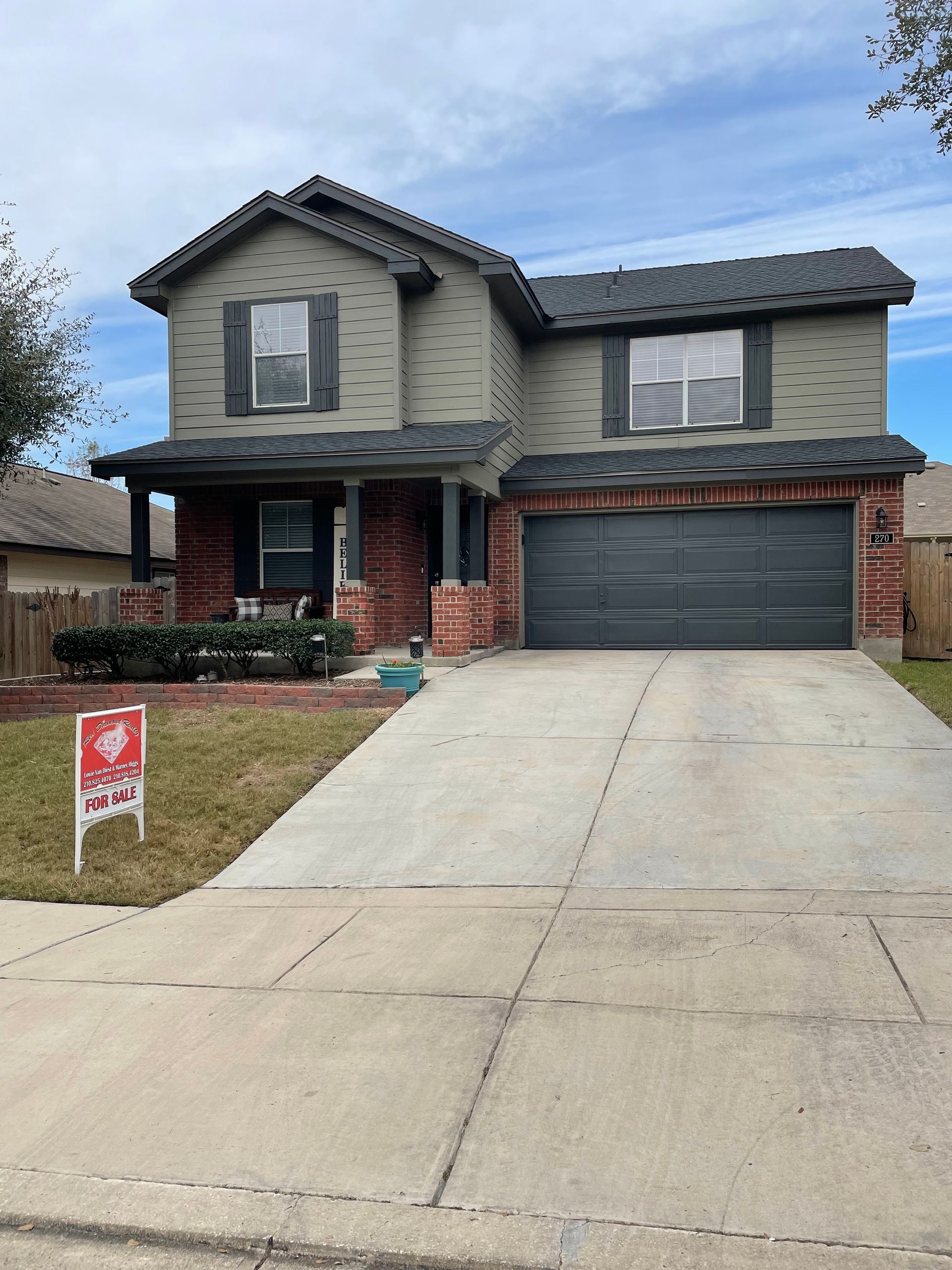 Two-story house with brick and gray siding, gray garage door, and a sign in front.