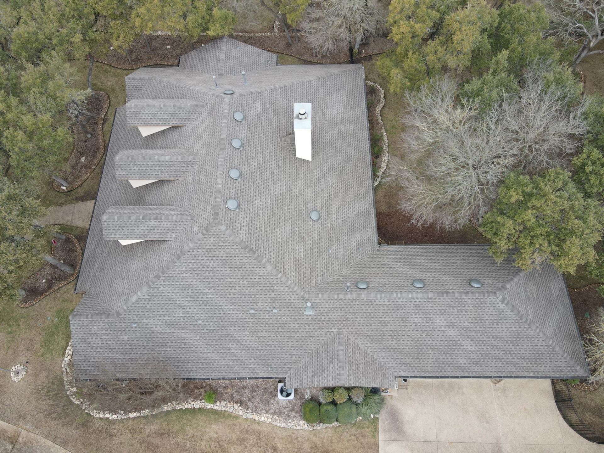 Overhead view of a house with a gray shingled roof, chimney, and surrounding trees.