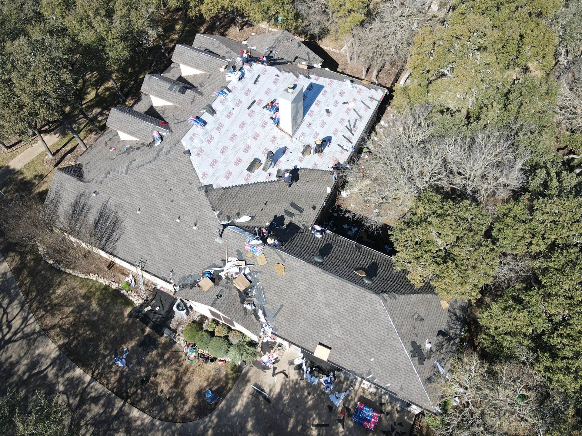 Aerial view of a house with a roof being repaired, surrounded by trees.
