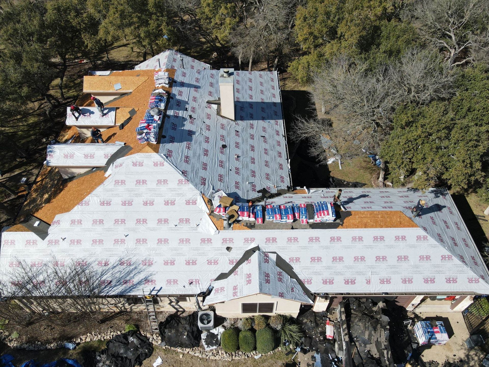 Aerial view of a house undergoing roof repair, with workers and materials visible on the roof.