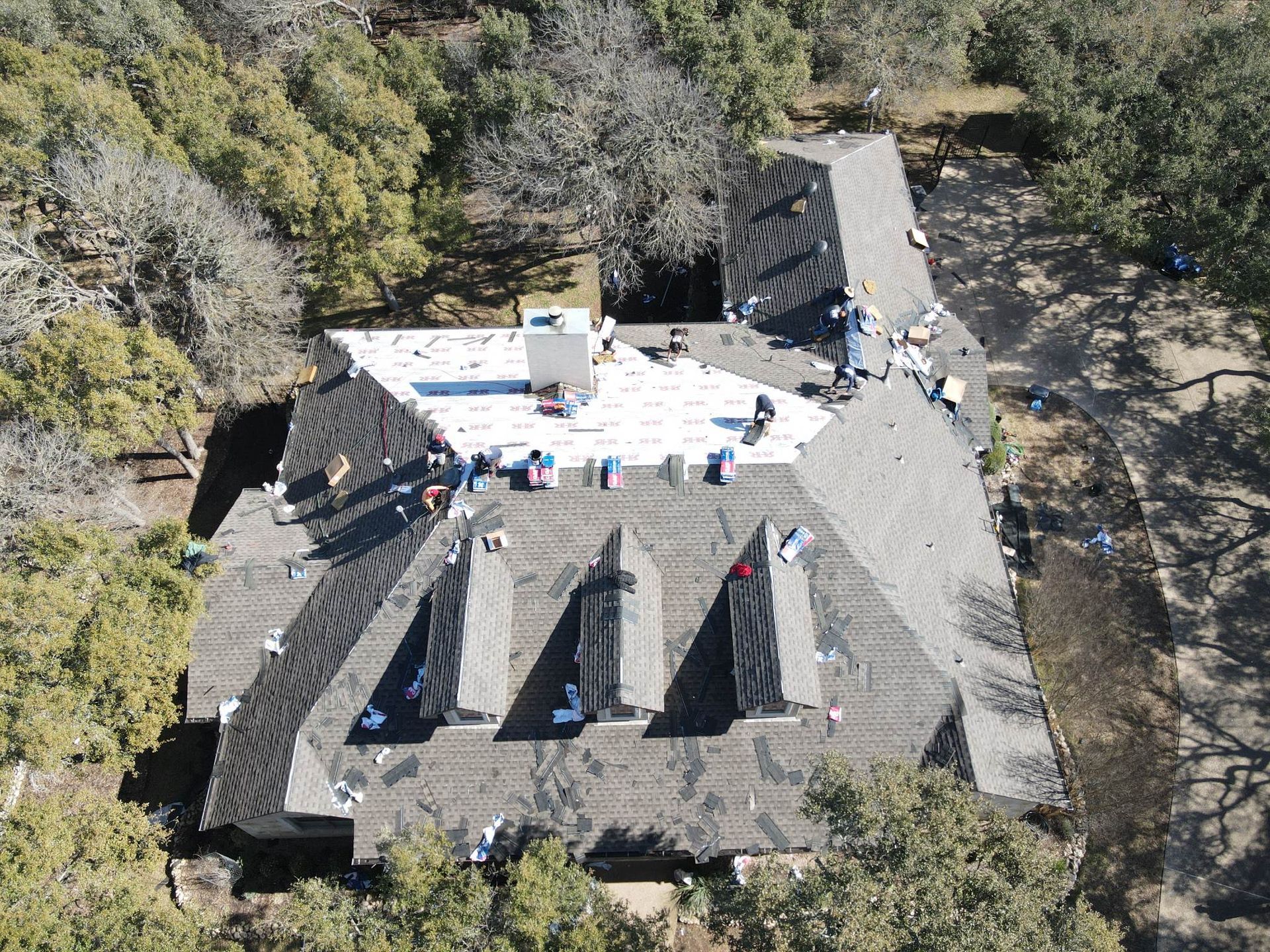Aerial view of roofers working on a house roof surrounded by trees.