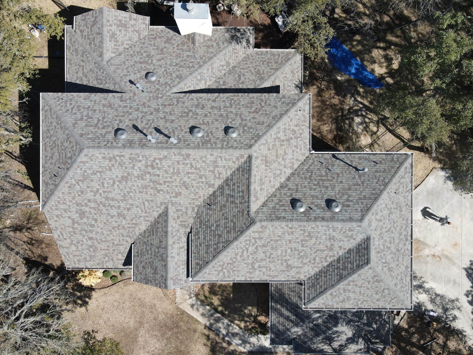 Aerial view of a house with a gray shingle roof surrounded by trees and a driveway.