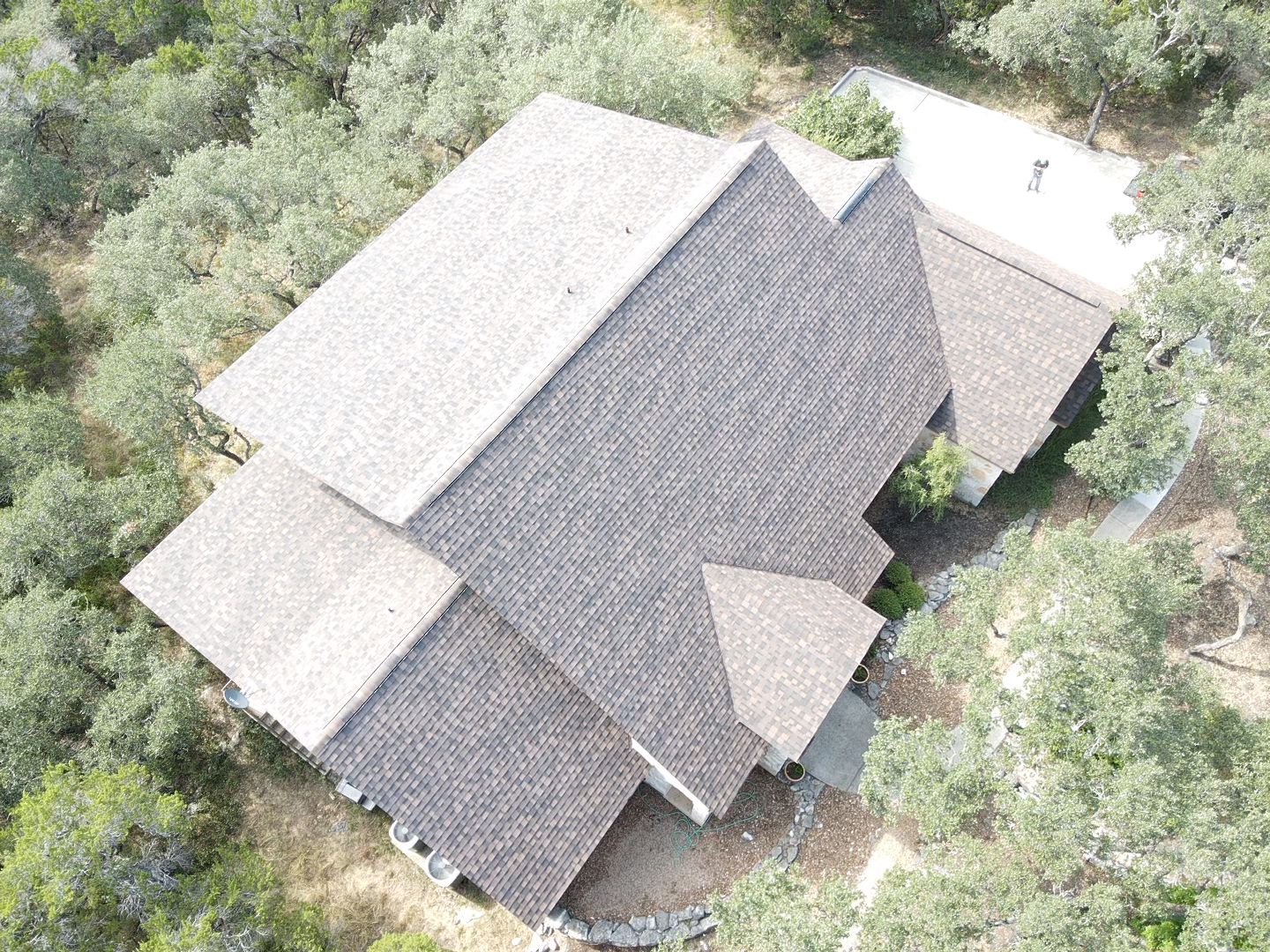 Overhead view of a house with a complex roof design, surrounded by trees.