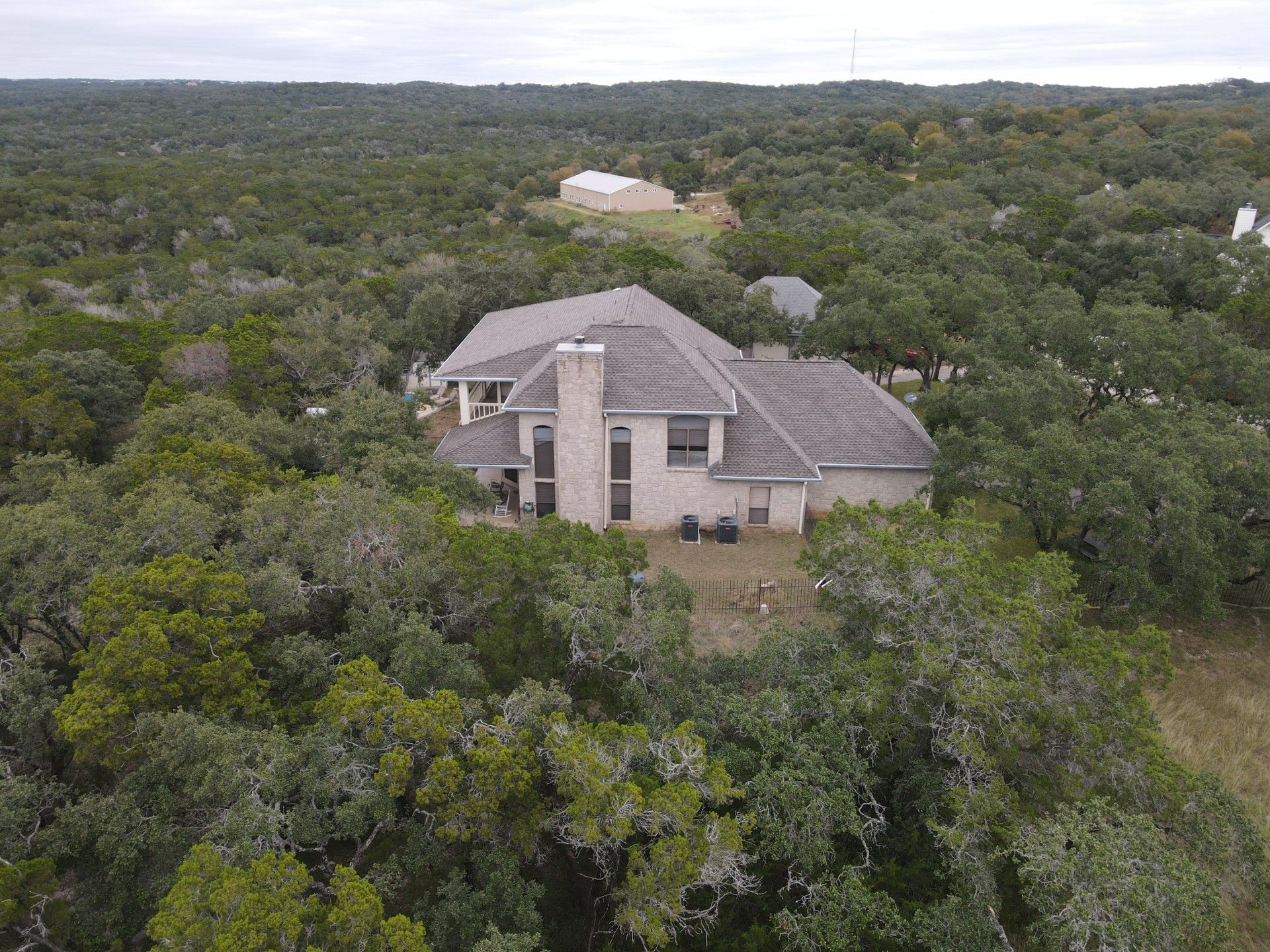 A house surrounded by dense trees in a wooded area on a cloudy day.