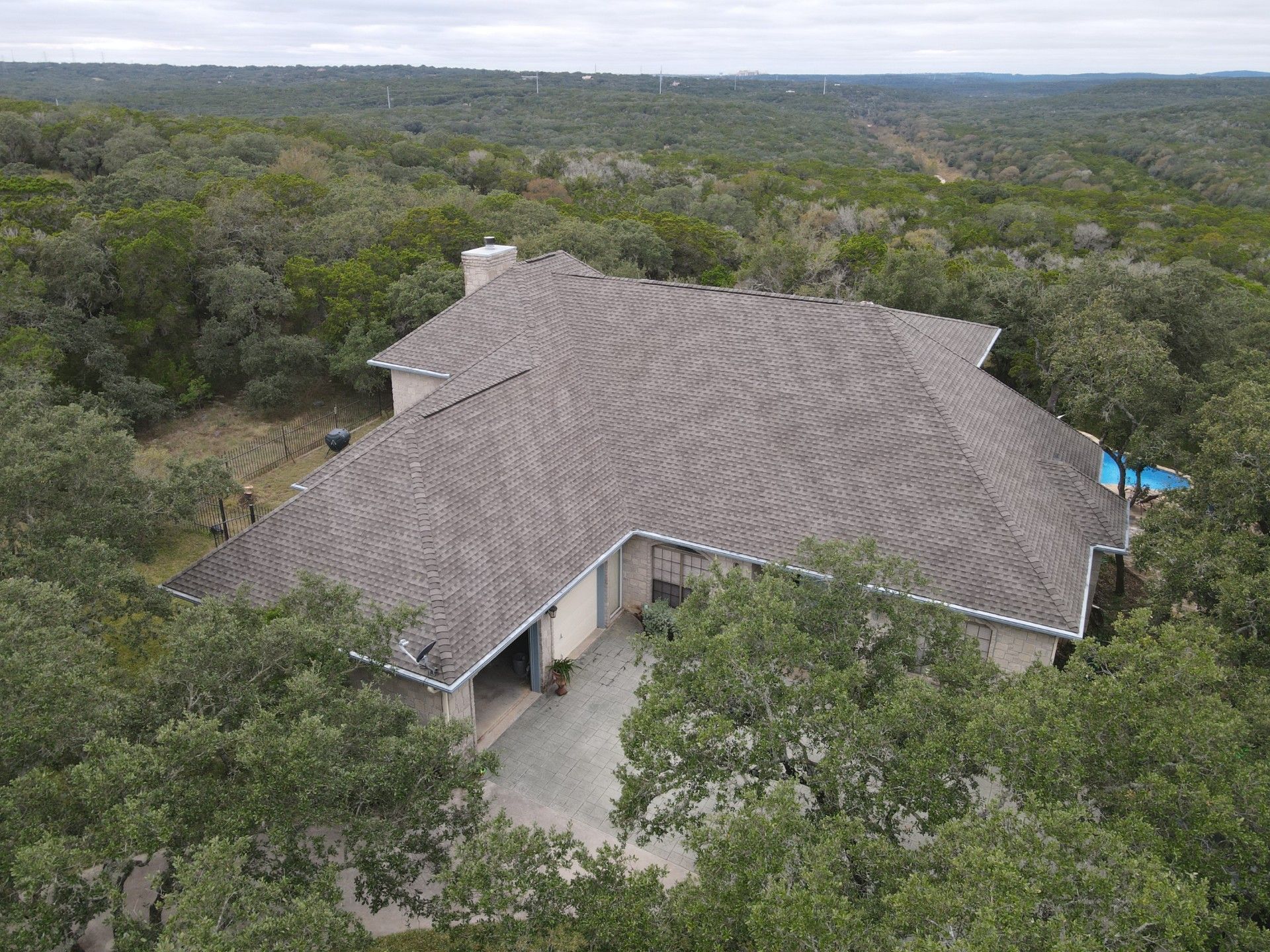 Aerial view of a house with a gray roof nestled amongst green trees in a wooded area.