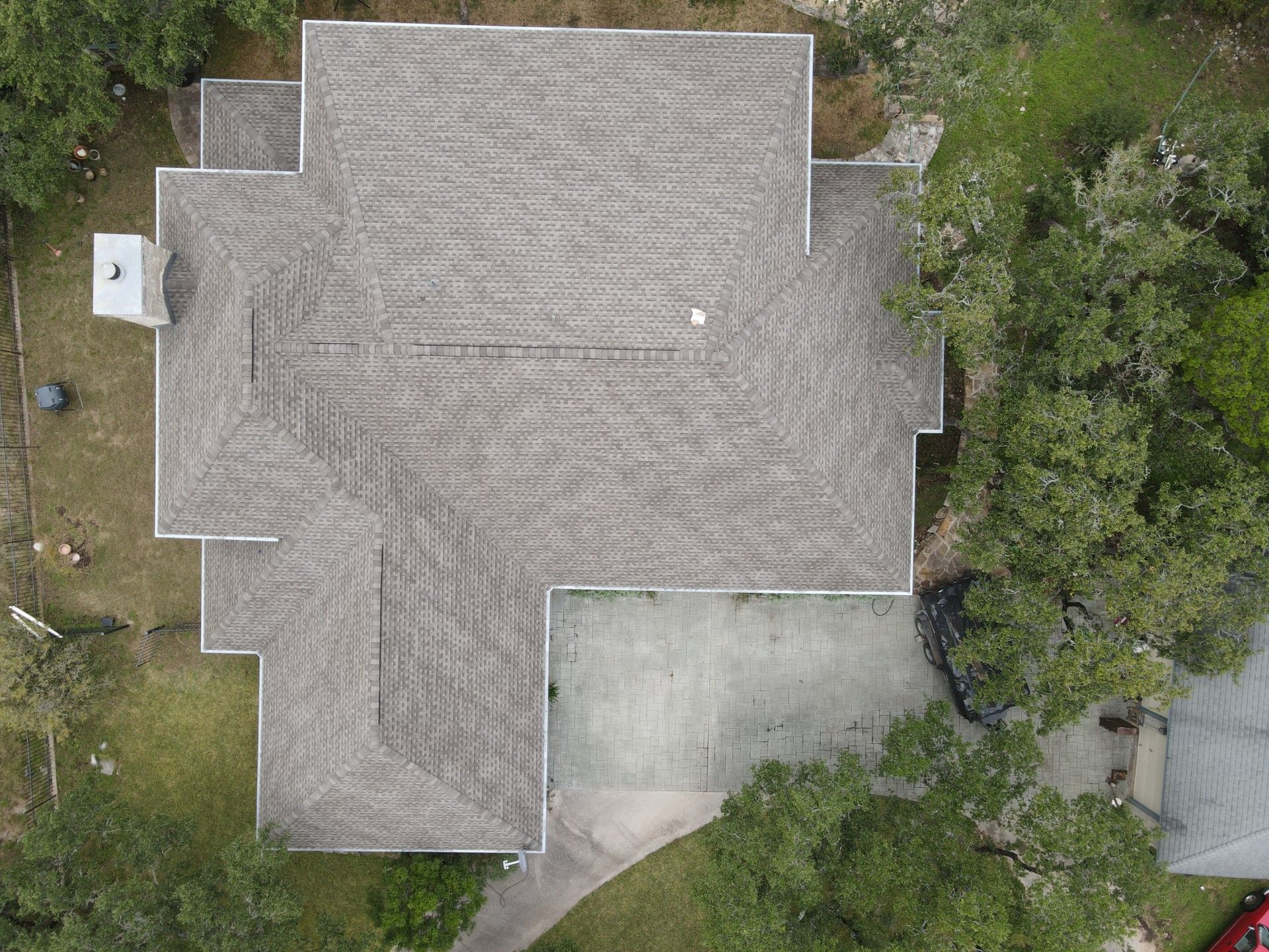 Overhead view of a house with a gray shingle roof and a driveway surrounded by trees.