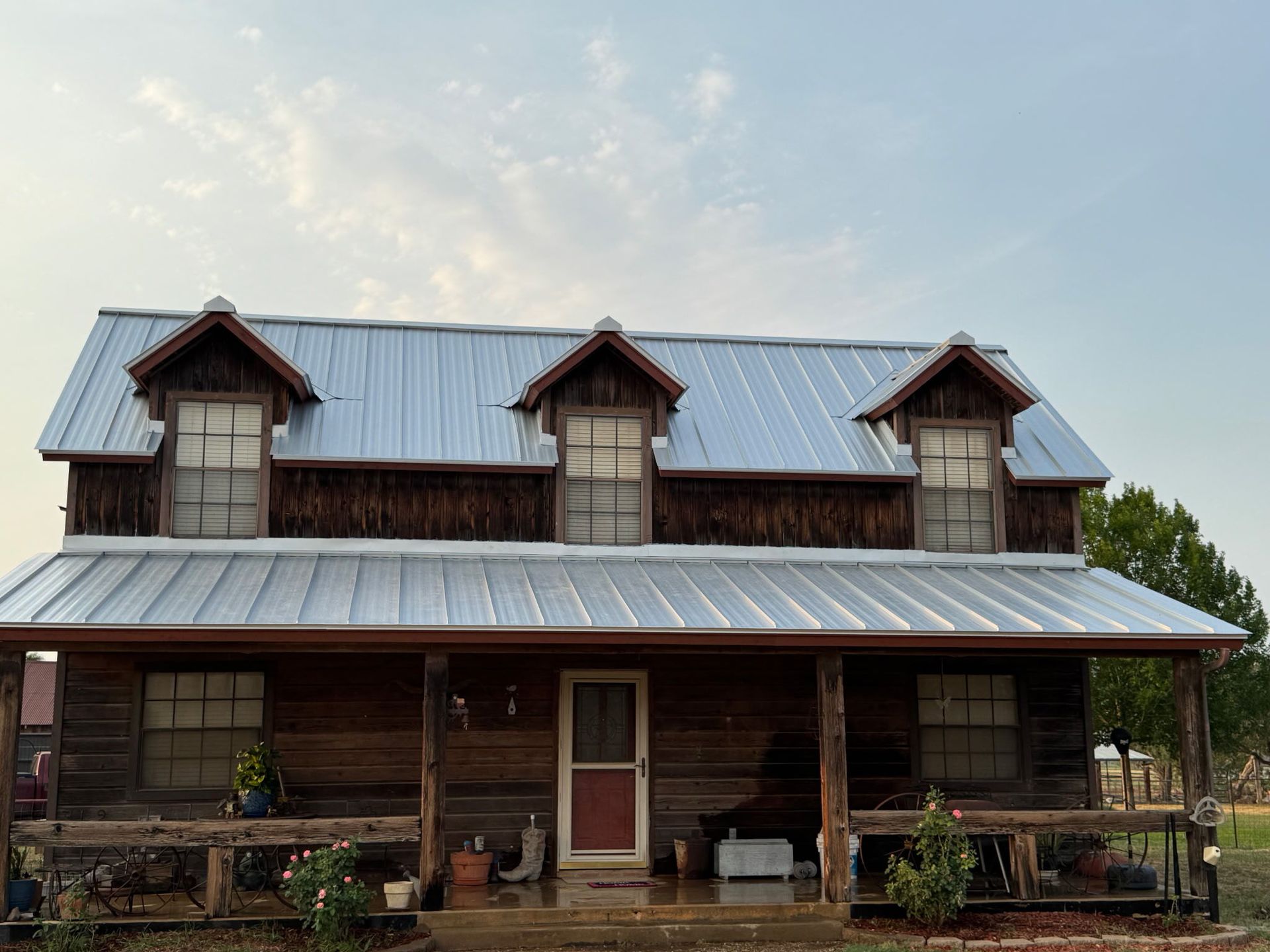 Rustic, two-story cabin with a porch, three dormer windows, and a metal roof.