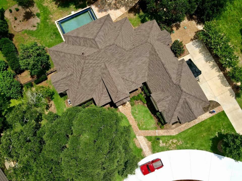 Aerial view of a large brown roof house with a pool, driveway, and red car.