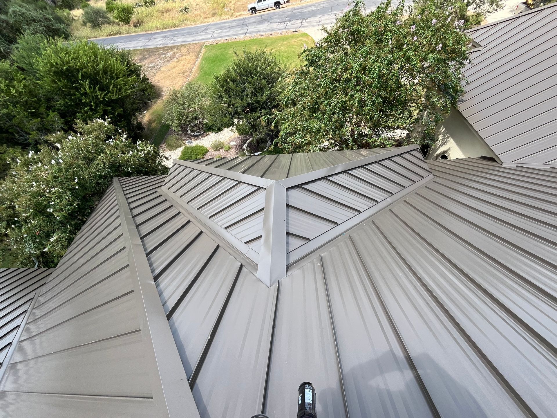 Gray metal roof with trees and a road in the background.