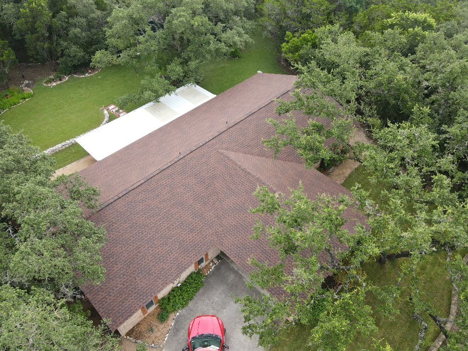 Overhead view of a brown roof house surrounded by green trees. A car is parked in the driveway.