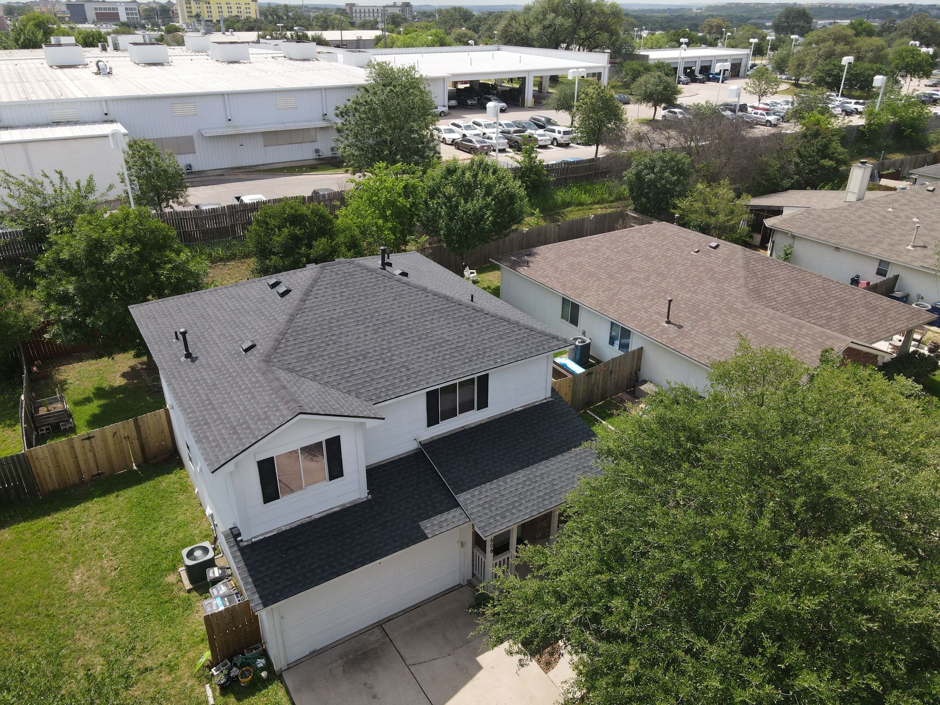 Aerial view of a two-story white house with a dark roof, trees, and surrounding homes in a suburban neighborhood.