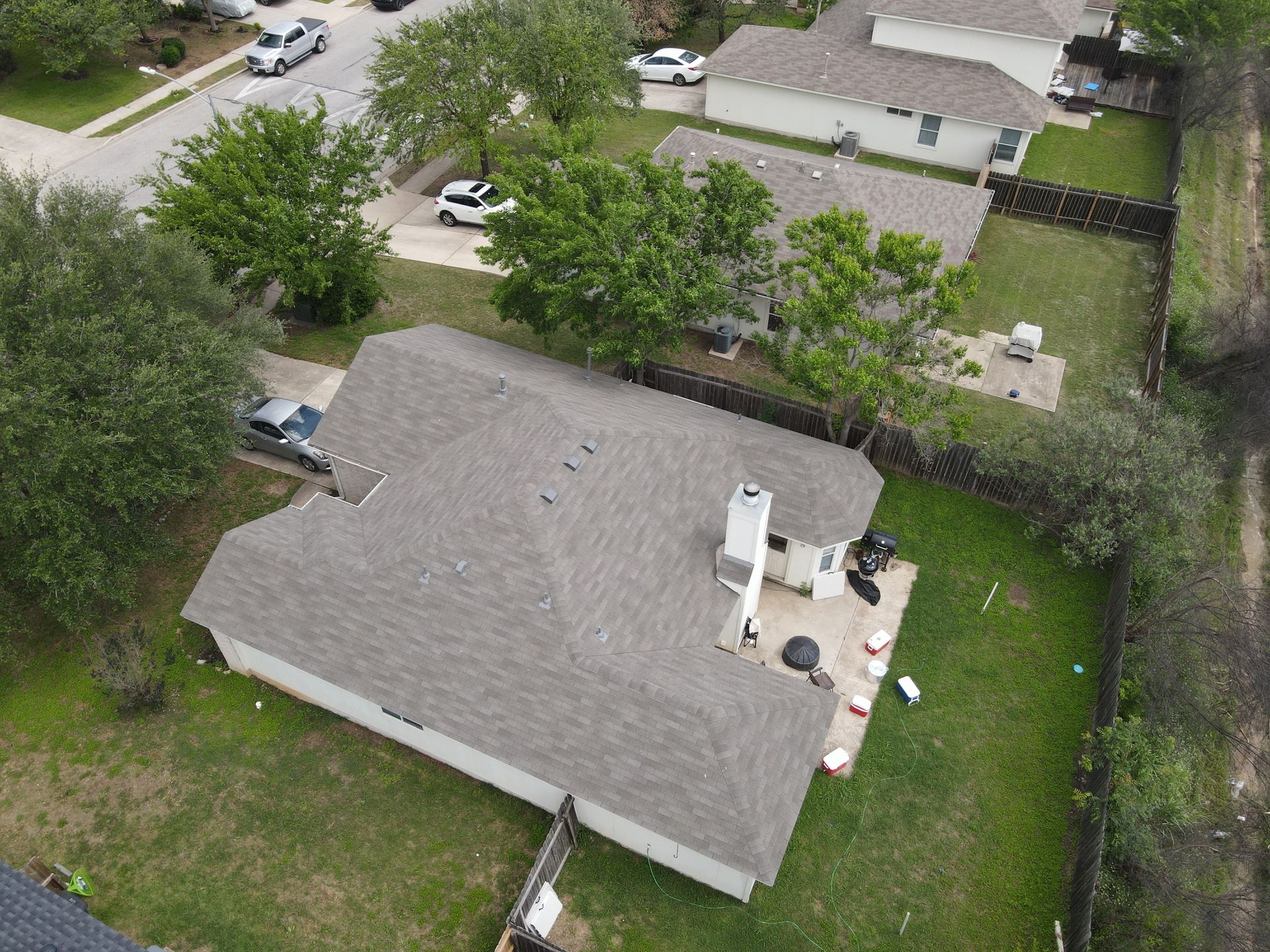 Aerial view of a house with a gray roof, green lawn, and backyard patio in a suburban neighborhood.
