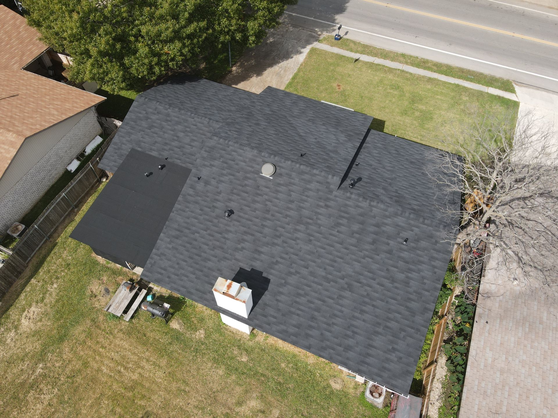 Overhead view of a house with a dark gray shingled roof and a white chimney.