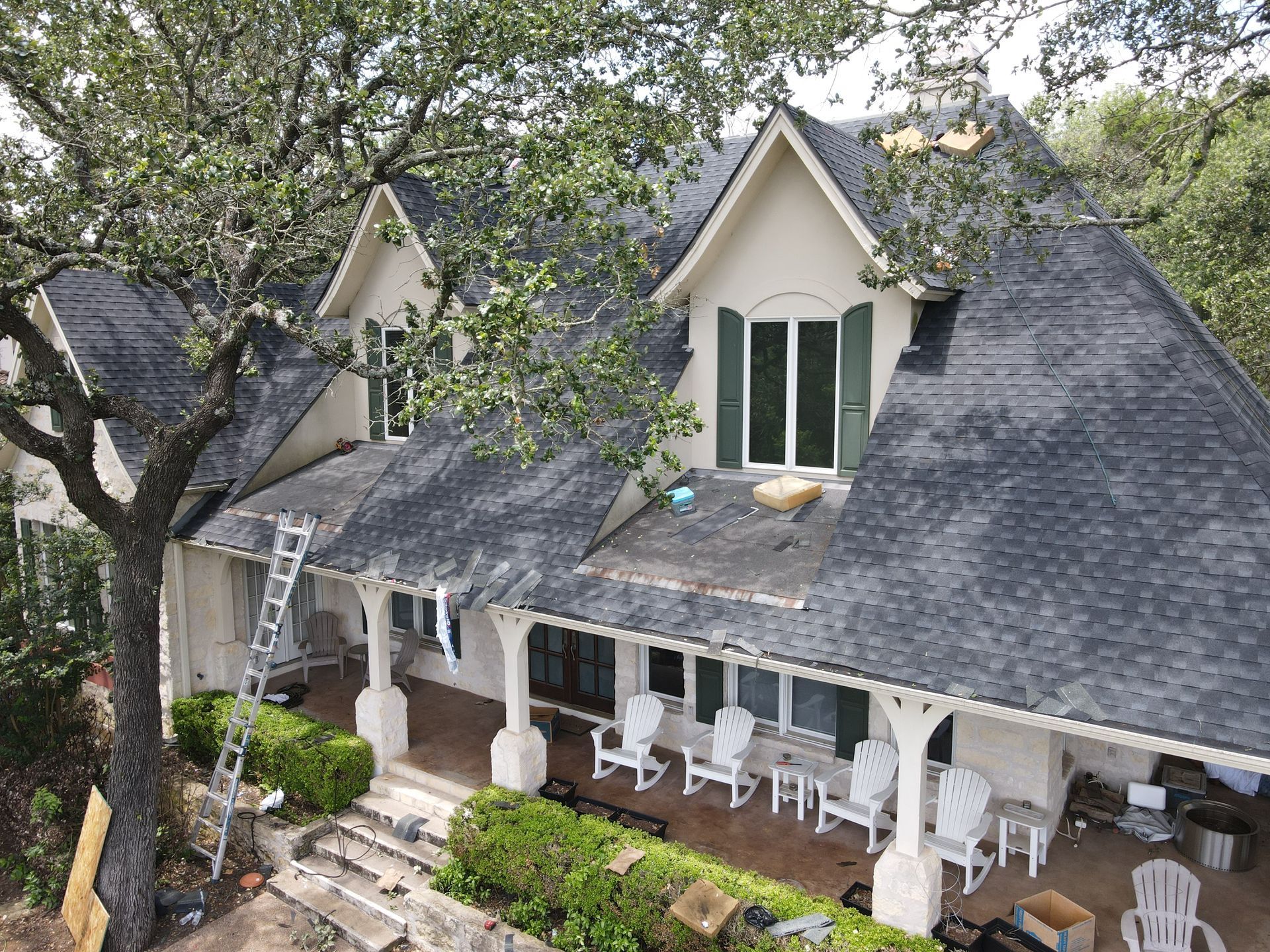 House under roof repair with ladder, tree, and outdoor seating.