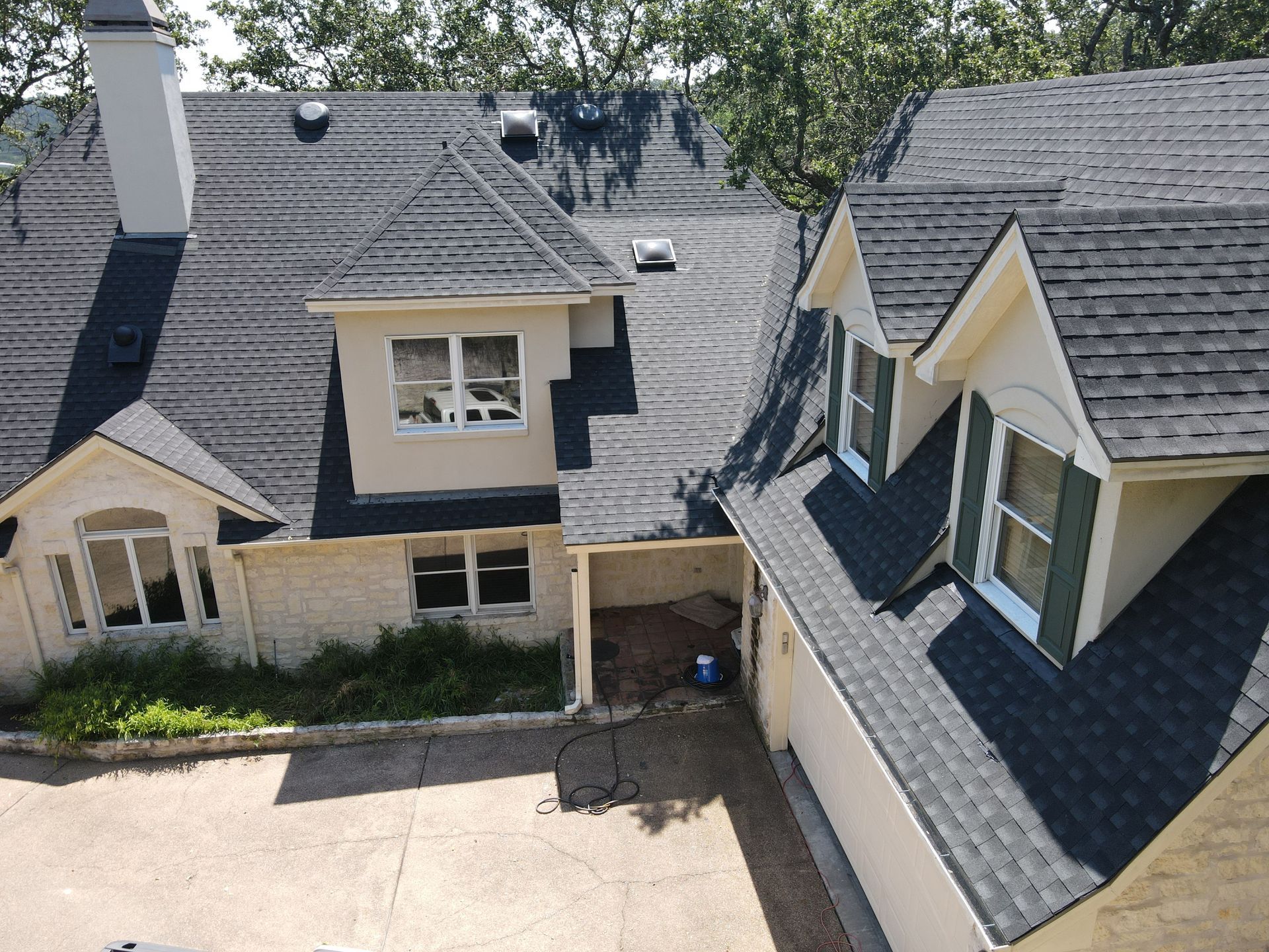 House with a dark gray shingled roof, beige walls, and green shutters.