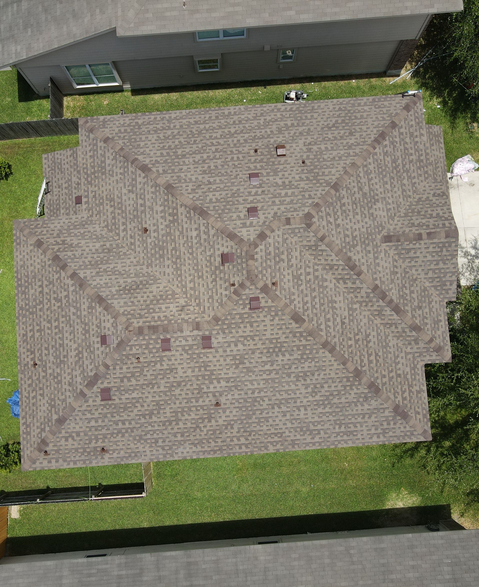 Overhead view of a brown shingled roof with several dark spots, likely indicating damage.