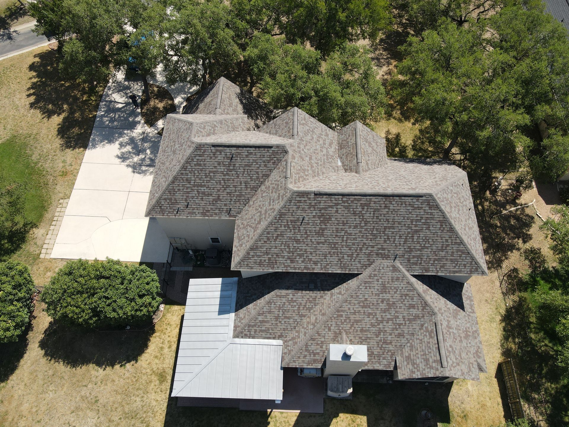 Aerial view of house with gray roof and concrete driveway, surrounded by trees.
