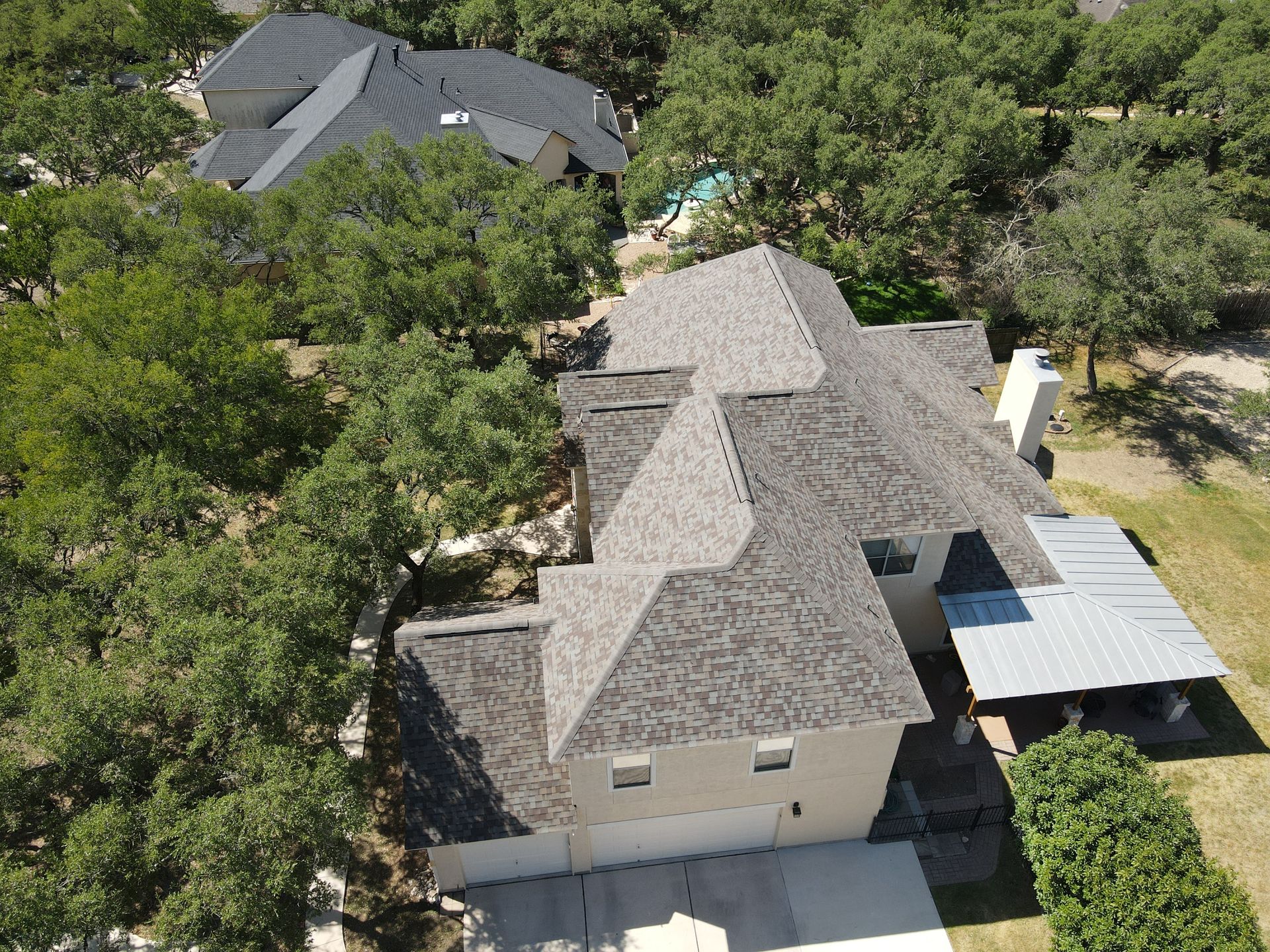 Overhead view of a house with a gray roof, surrounded by trees, and a detached metal carport on the right.