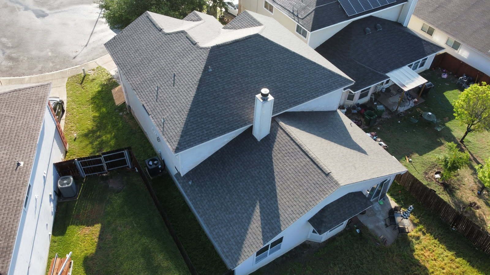 Overhead view of a gray-roofed house with a chimney, set in a grassy yard; another house is visible nearby.