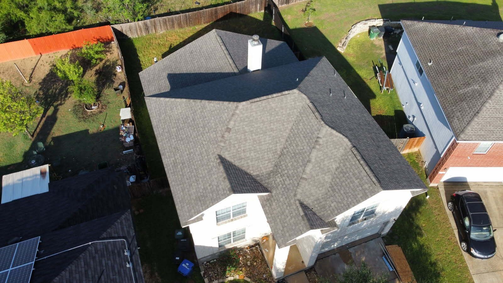 Aerial view of a house with a gray roof, white siding, and a black car in the driveway.