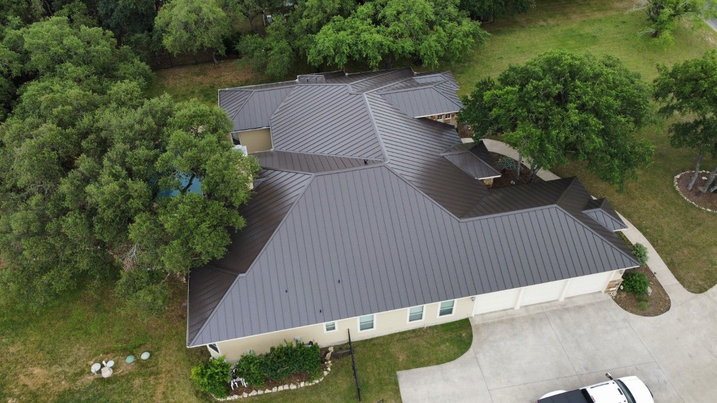 Overhead view of a house with a dark roof surrounded by trees and a driveway.