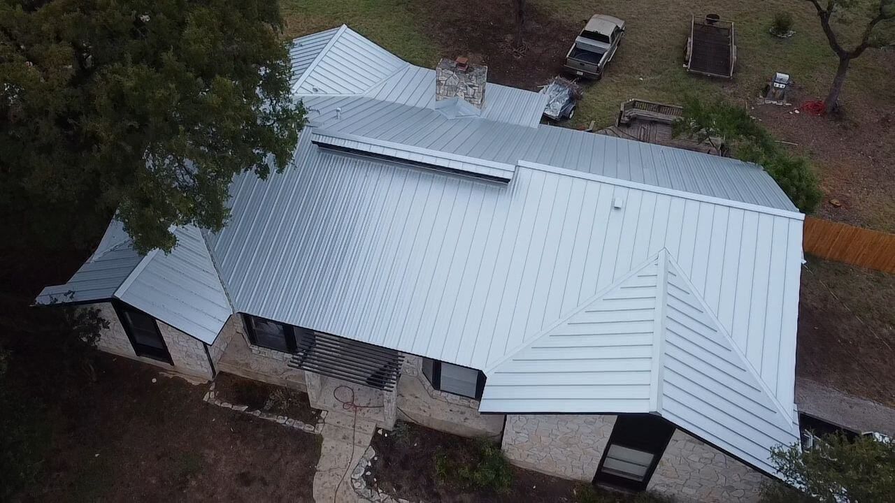 Overhead view of a house with a silver metal roof and stone exterior, surrounded by trees and a yard.