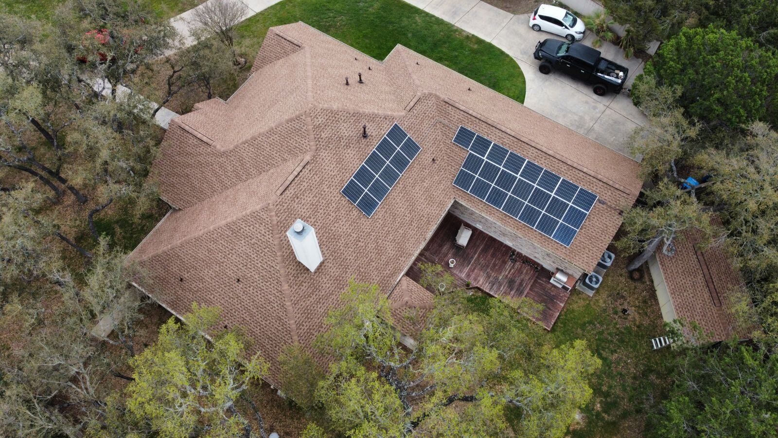 Overhead view of a house with solar panels on the roof, surrounded by trees and with vehicles in the driveway.