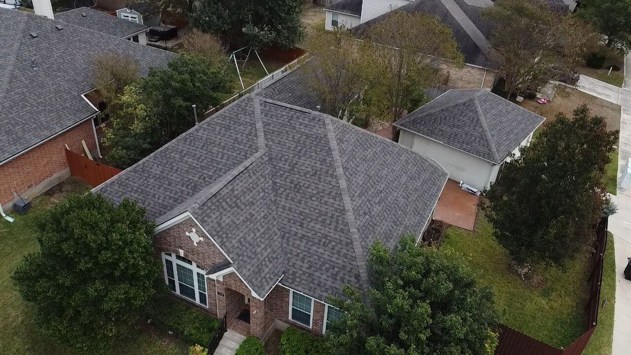 Aerial view of a house with a gray roof and surrounding trees in a residential neighborhood.