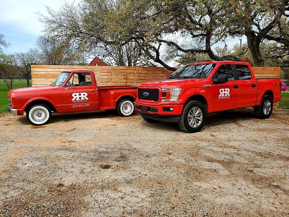 Two red pickup trucks parked on gravel. One is vintage, the other modern. Both have white logos.