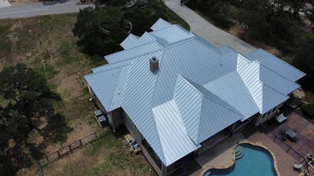 Aerial view of a large house with a silver metal roof, a pool, and a grassy yard.