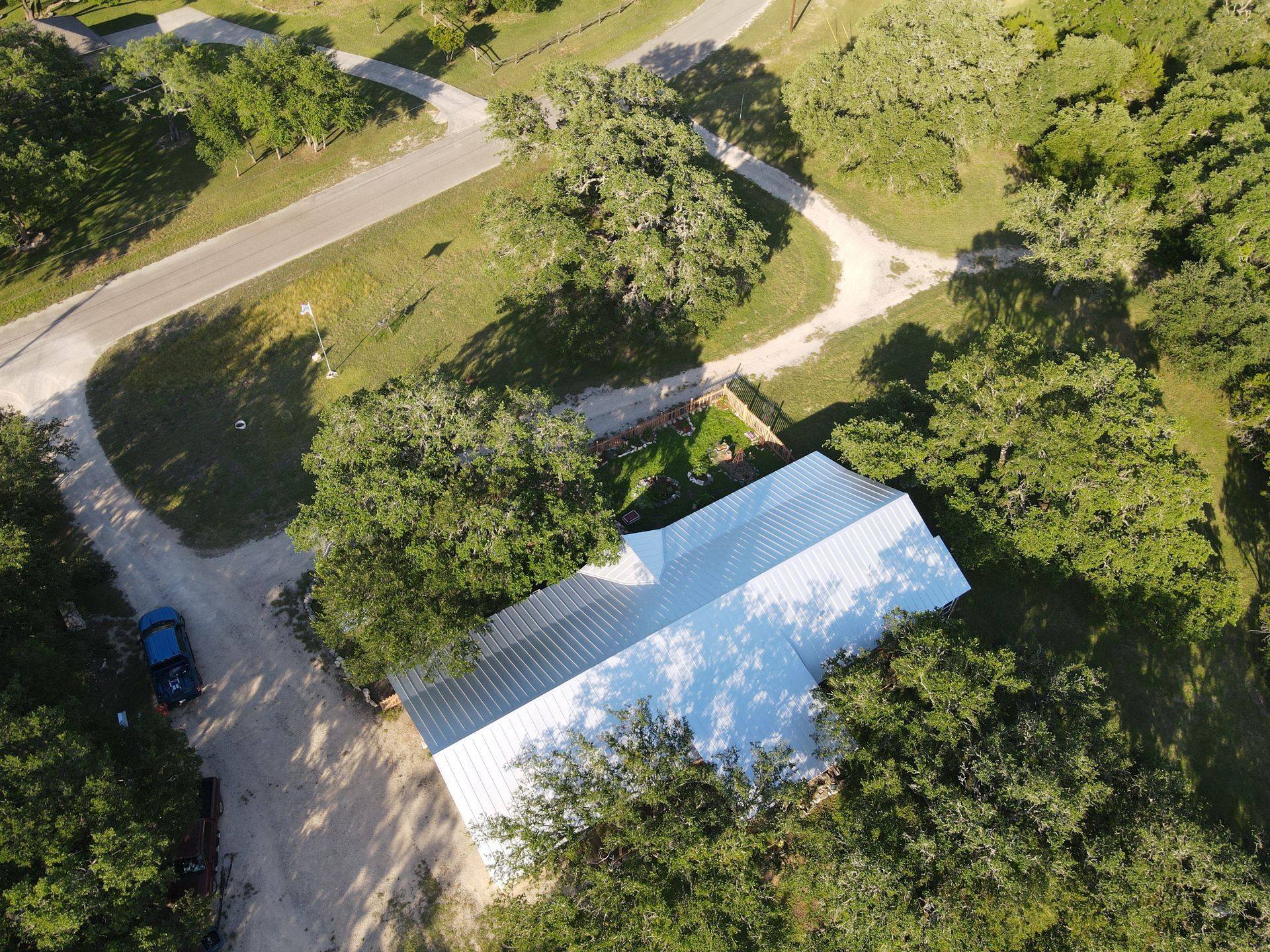 Aerial view of a house with a white roof surrounded by trees and roads.