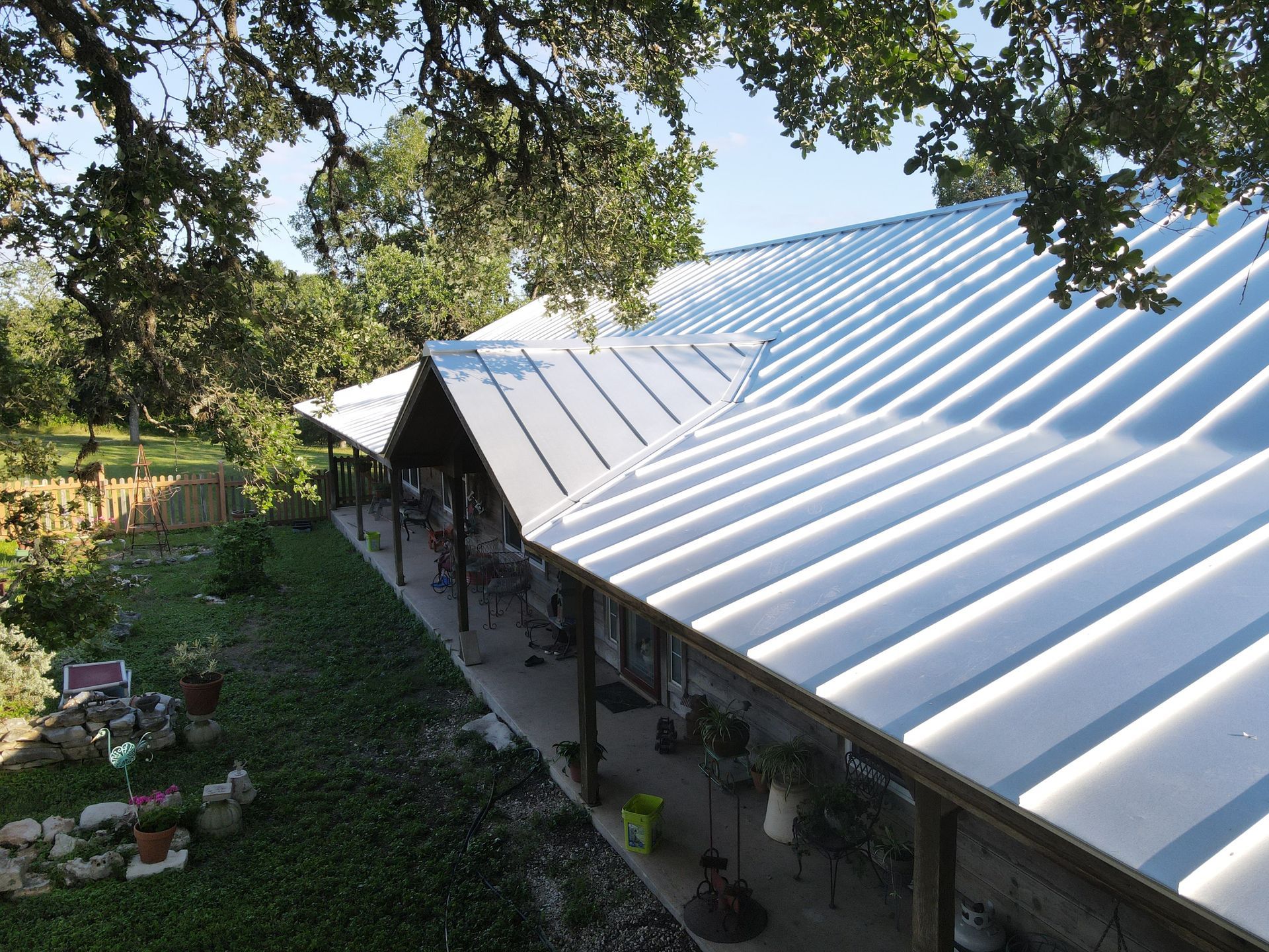 Metal roof of a house, extending over a porch, surrounded by trees and greenery.