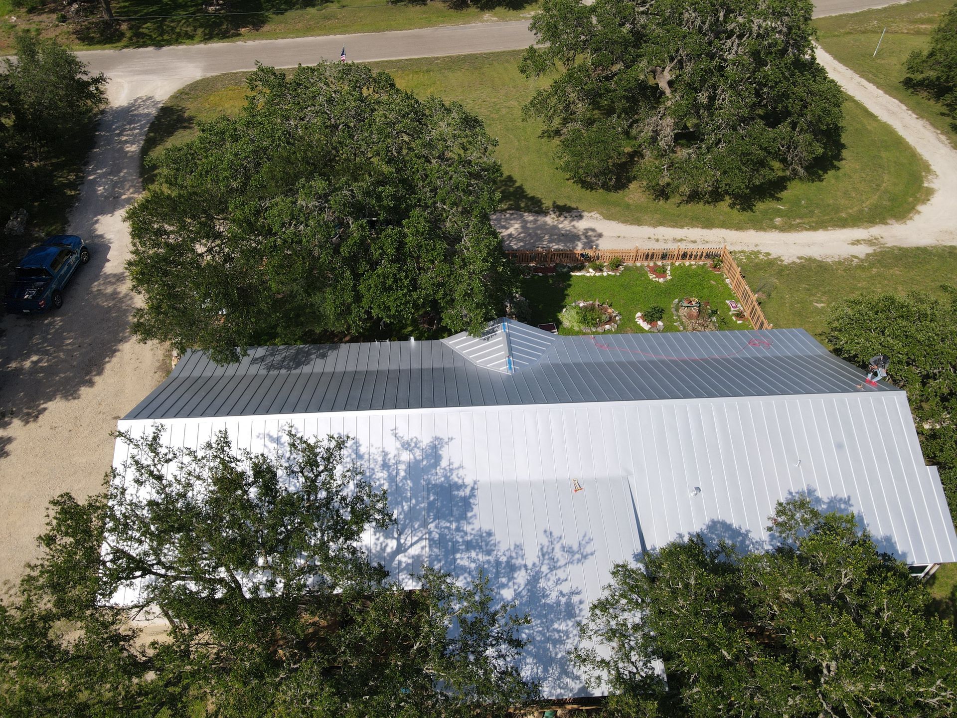 Aerial view of a house with a silver metal roof, surrounded by trees and a small garden.