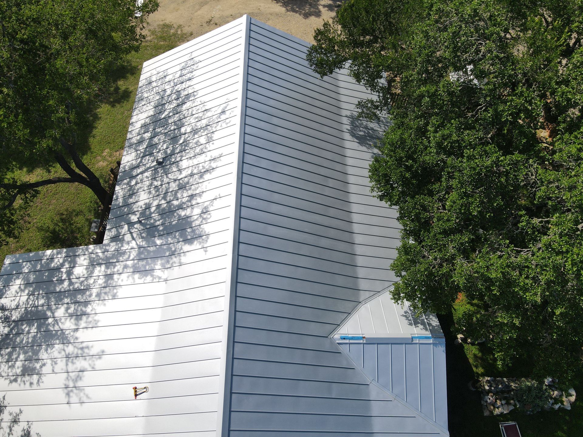 Aerial view of a building with a silver metal roof and trees casting shadows.