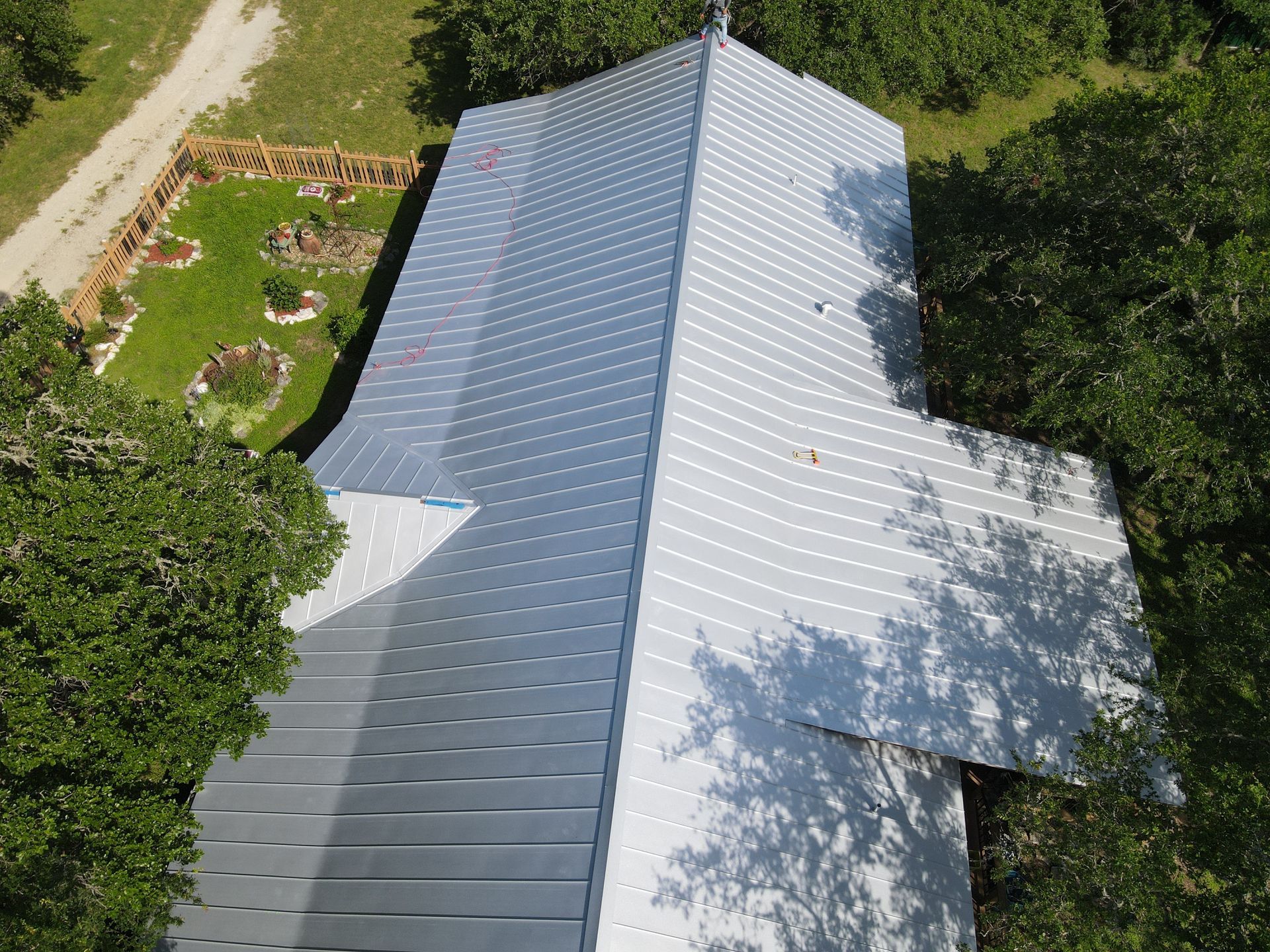 Aerial view of a gray metal roof on a building, surrounded by green trees and grass.