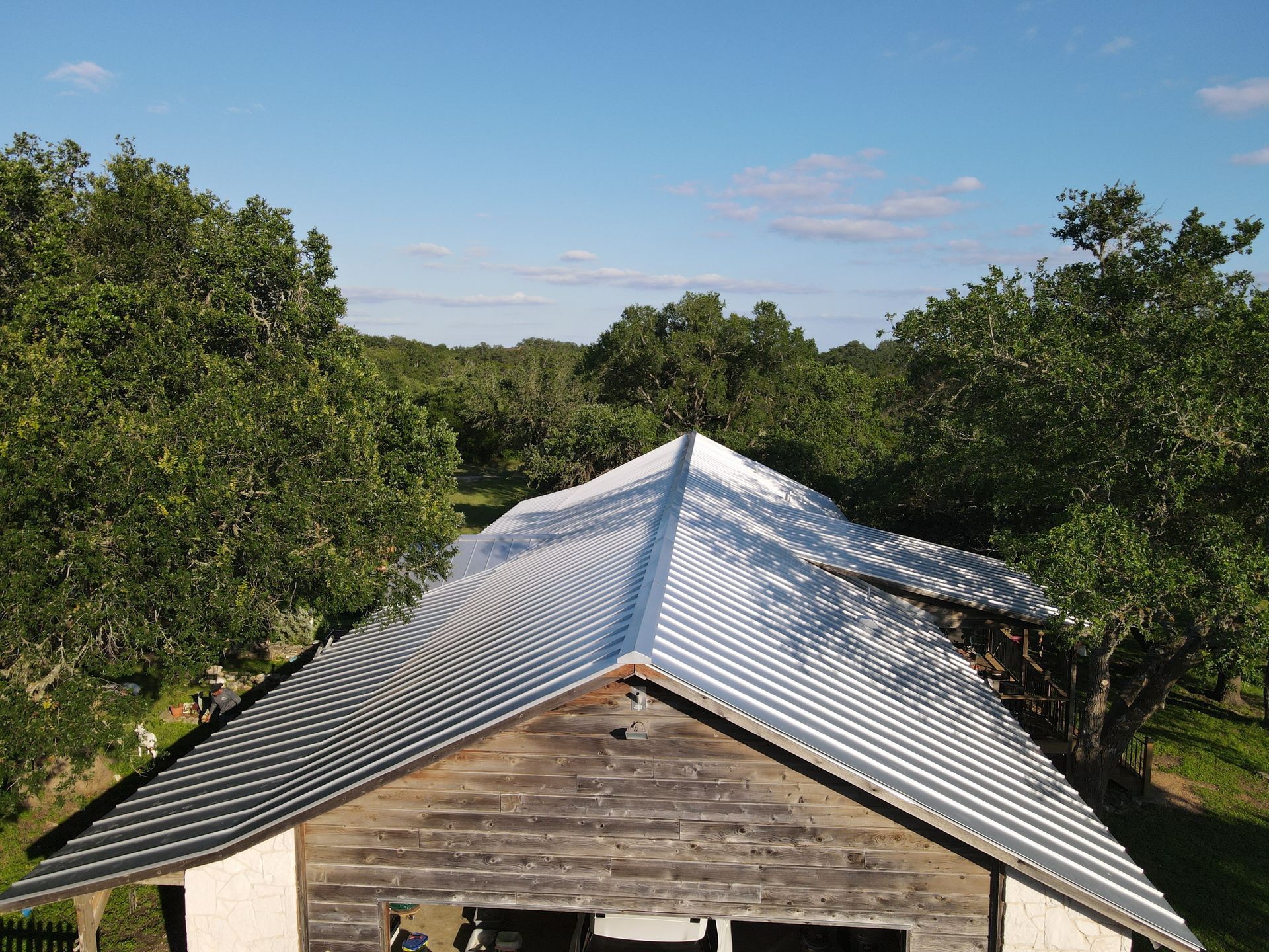 Old wooden building with a corrugated metal roof surrounded by trees under a blue sky.