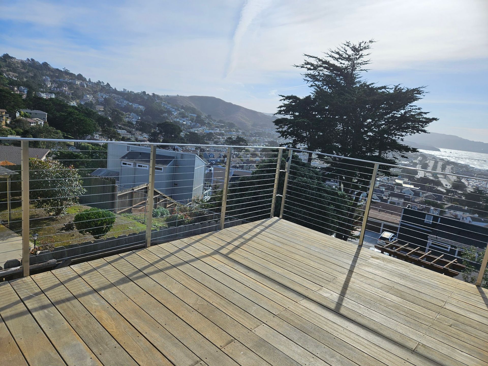 A wooden deck with a stainless steel railing overlooking a city