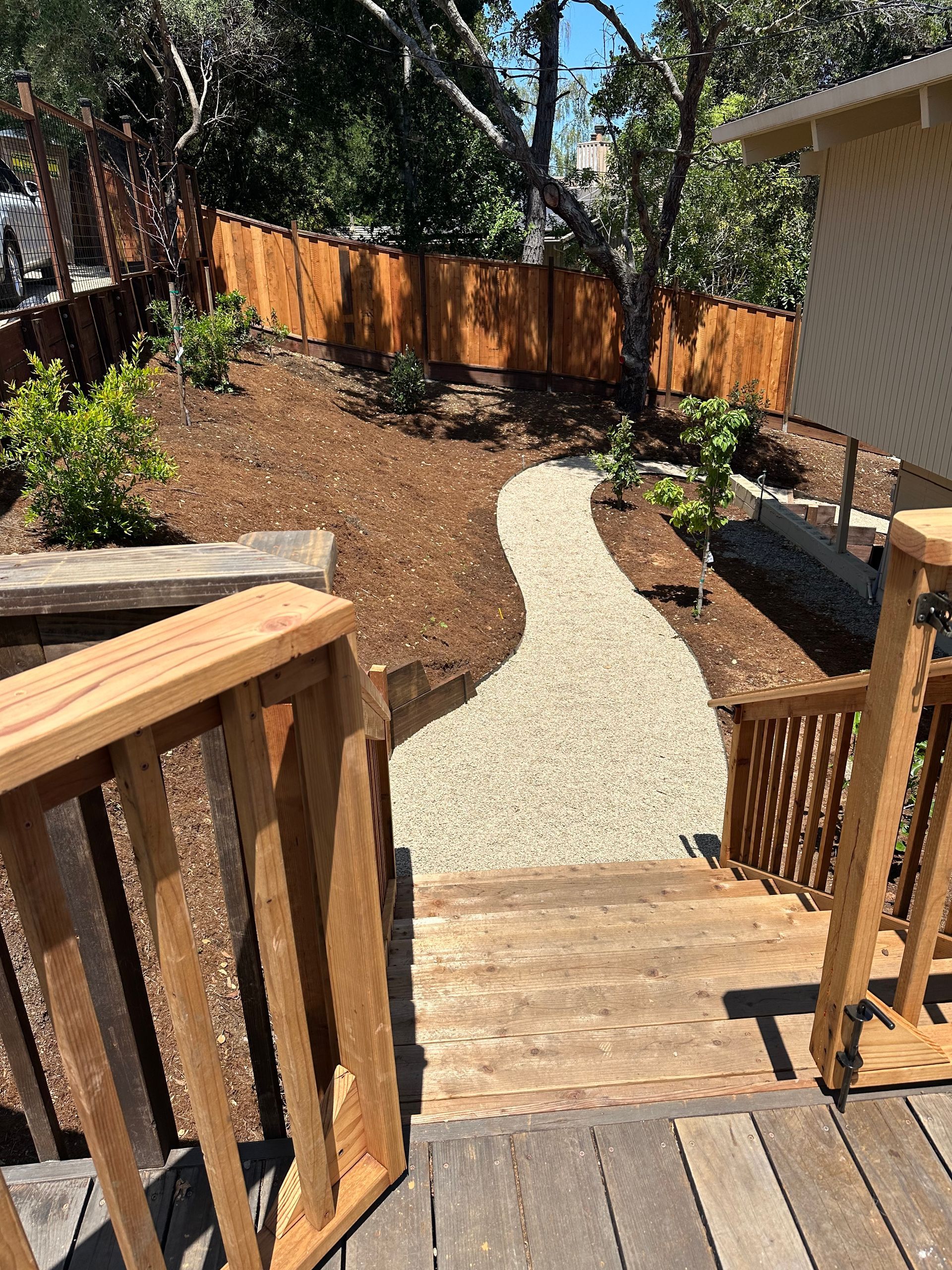 A wooden deck with stairs leading up to a path in the backyard.