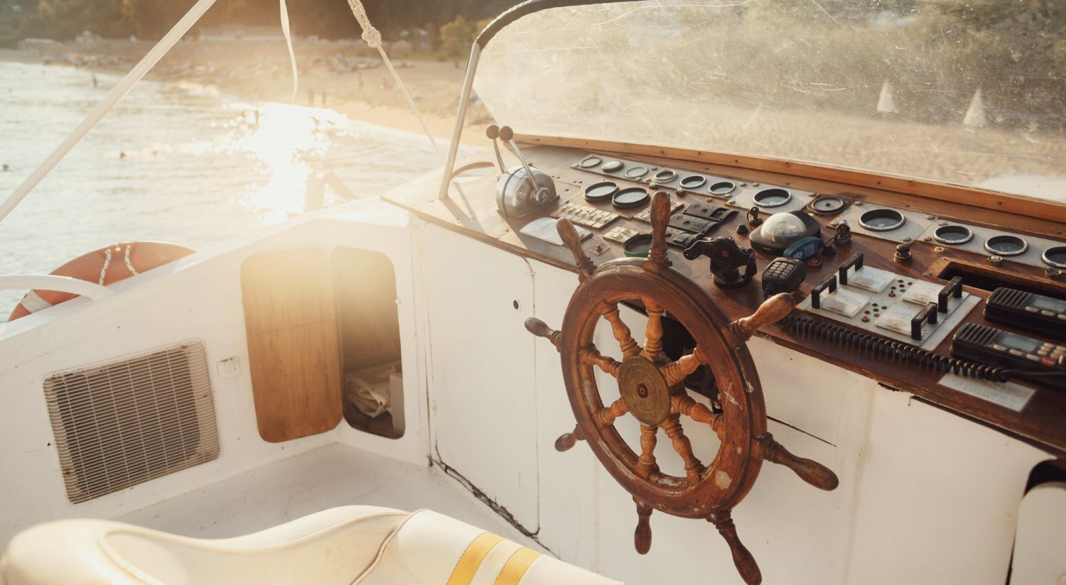 A wooden steering wheel is on the dashboard of a boat.