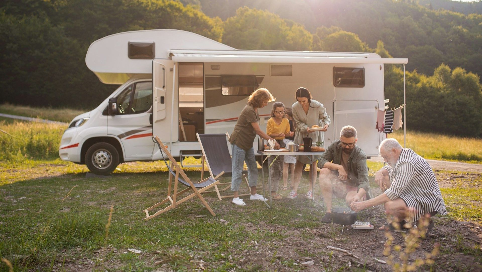 A group of people are sitting around a campfire in front of a rv.