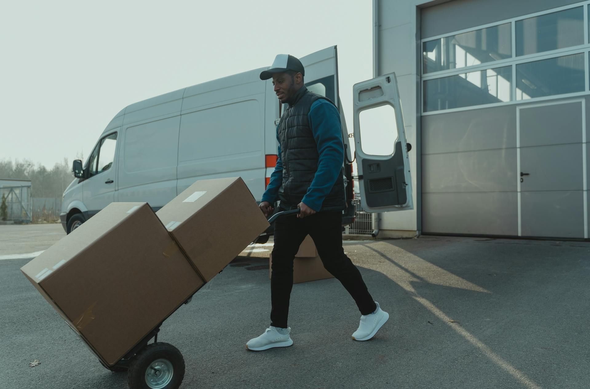 A man is pushing a cart with boxes in front of a van.