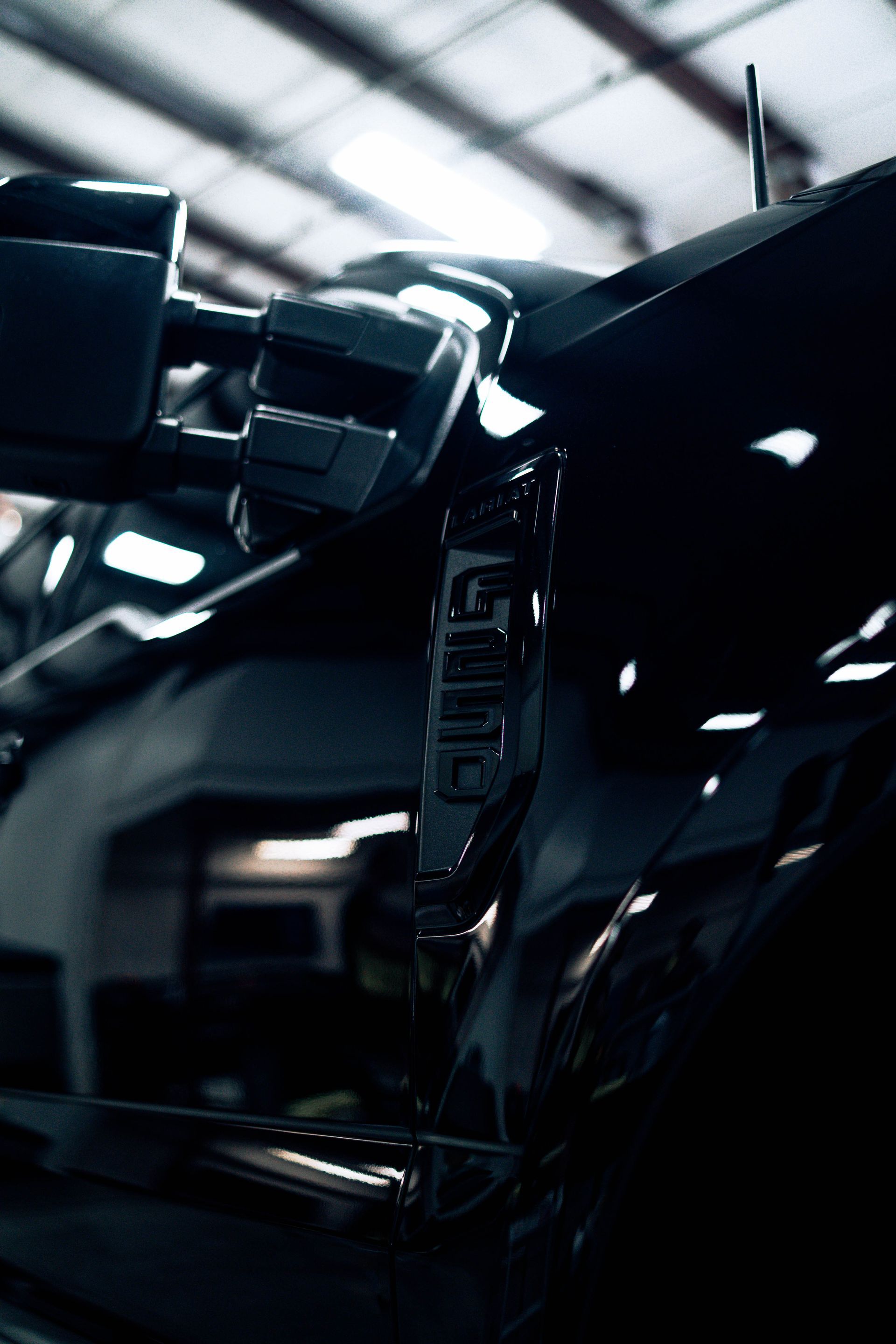Close-up of a sleek black sports car in a dim industrial garage, with bright overhead lights reflecting off its body