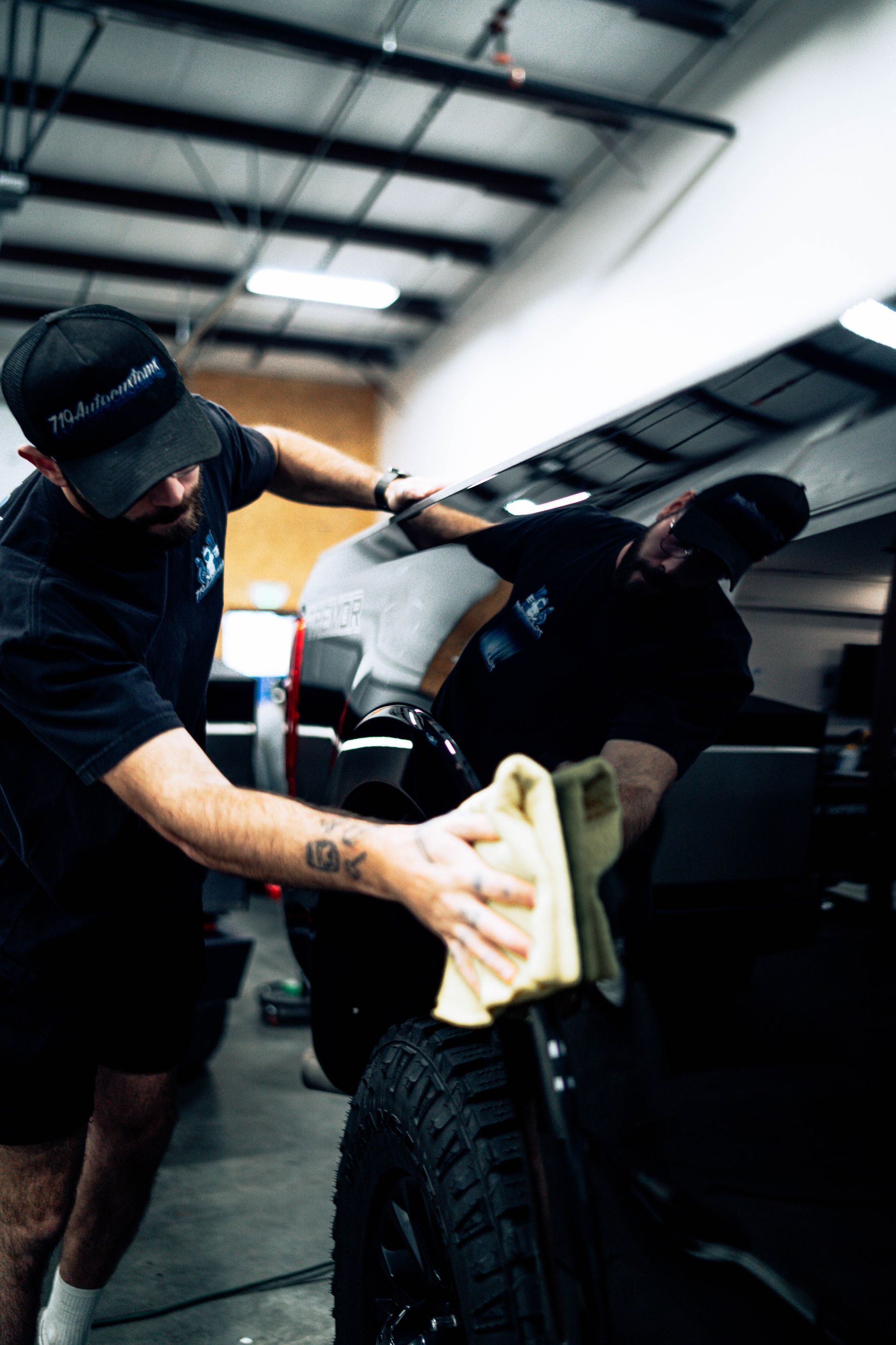 Two mechanics cleaning a black car in a garage with a cloth and spray bottle